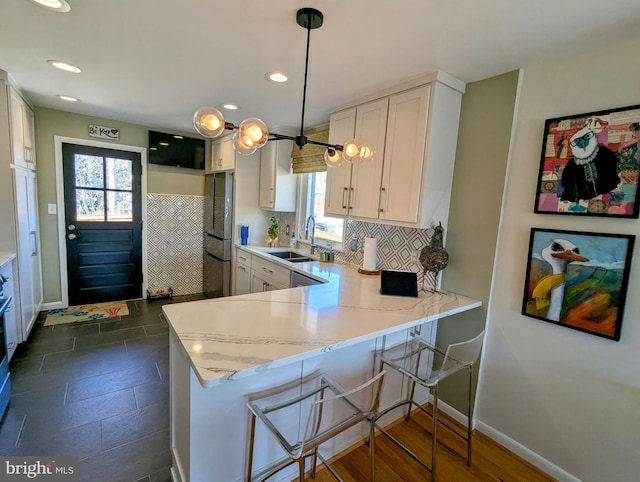 kitchen with a peninsula, white cabinetry, a sink, and decorative light fixtures