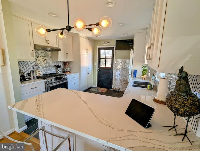 kitchen featuring a peninsula, a sink, a kitchen breakfast bar, white cabinets, and gas range