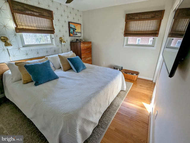 bedroom with an accent wall, baseboards, wood finished floors, and multiple windows