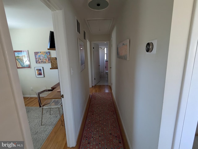 corridor with light wood-style flooring, attic access, and baseboards