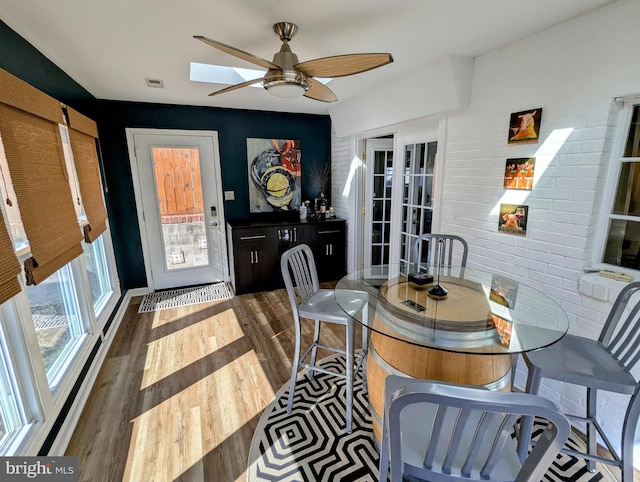 dining room featuring dark wood-style floors, brick wall, visible vents, and ceiling fan