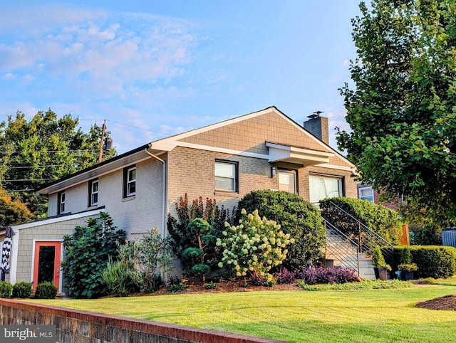 view of front of house featuring an attached garage, brick siding, a chimney, and a front yard