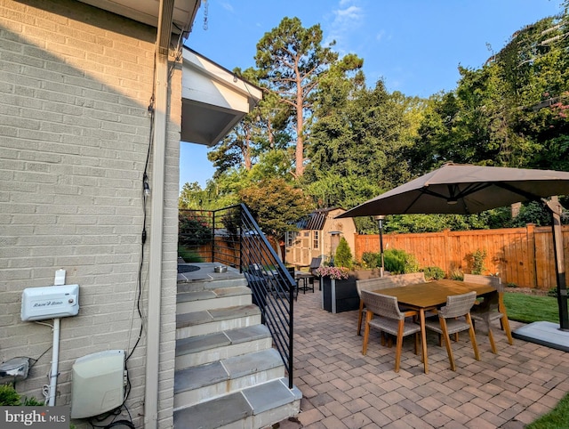 view of patio / terrace featuring a storage shed, a fenced backyard, an outbuilding, stairs, and outdoor dining area