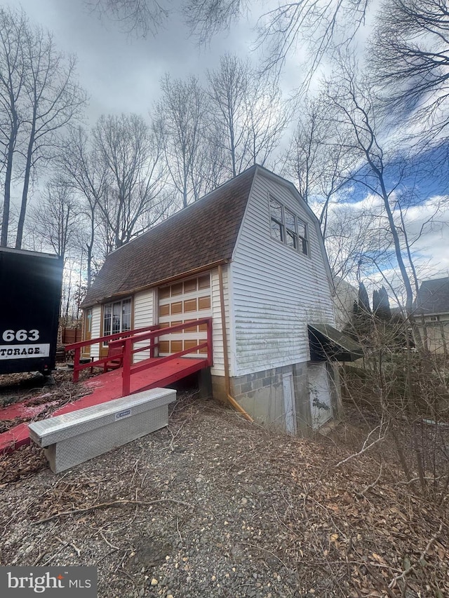 view of side of home featuring a deck, a gambrel roof, and roof with shingles