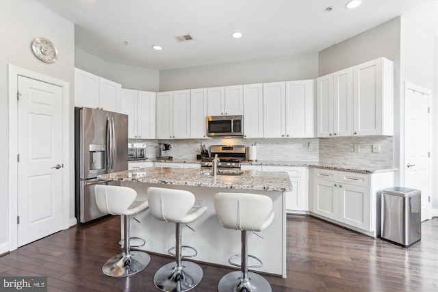 kitchen with stainless steel appliances, a breakfast bar, dark wood-style flooring, white cabinets, and light stone countertops