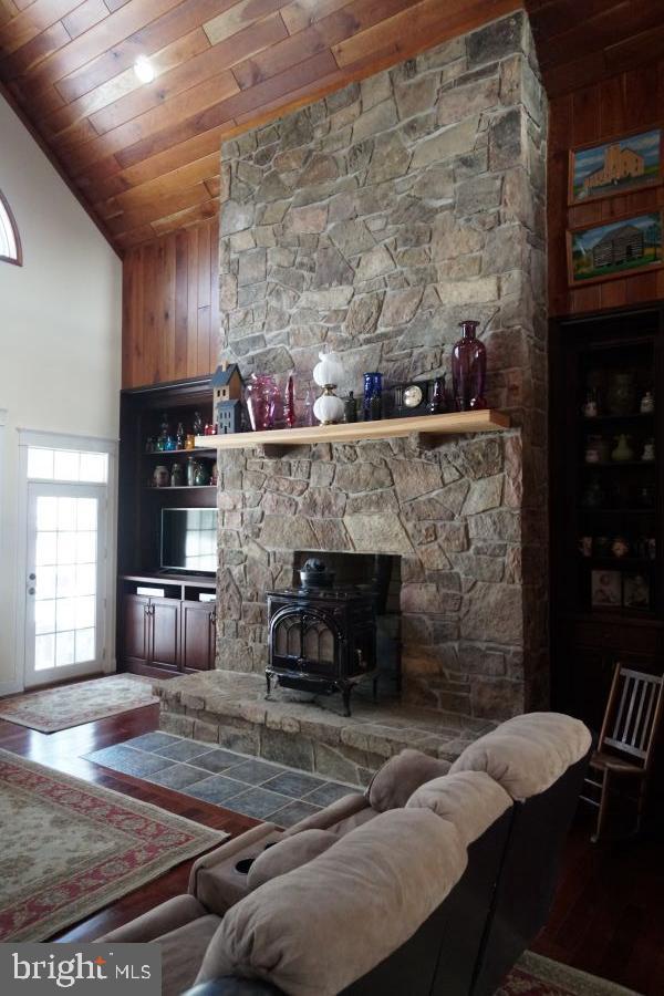 living area featuring a wood stove, wooden ceiling, high vaulted ceiling, and wood walls