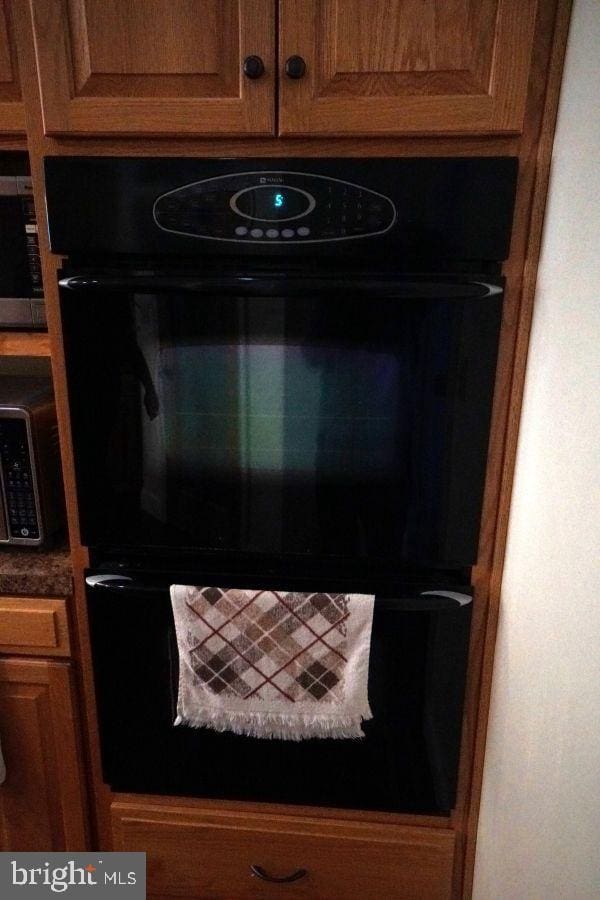 details with stainless steel microwave, brown cabinetry, and dobule oven black