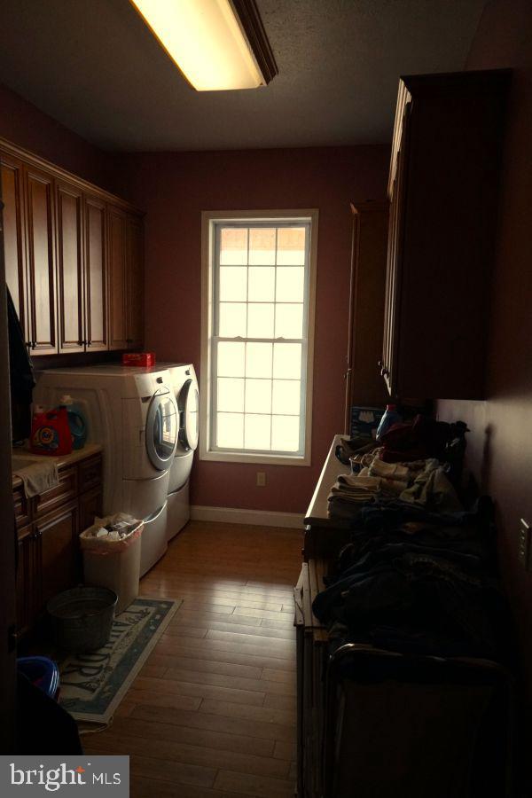 laundry area with light wood-type flooring, cabinet space, washing machine and dryer, and baseboards