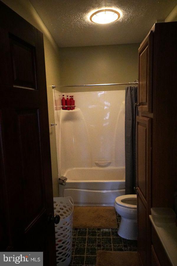 full bathroom featuring a textured ceiling, shower / bath combination with curtain, and toilet