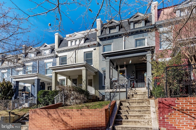 view of front of property featuring brick siding, mansard roof, a porch, stairway, and a high end roof