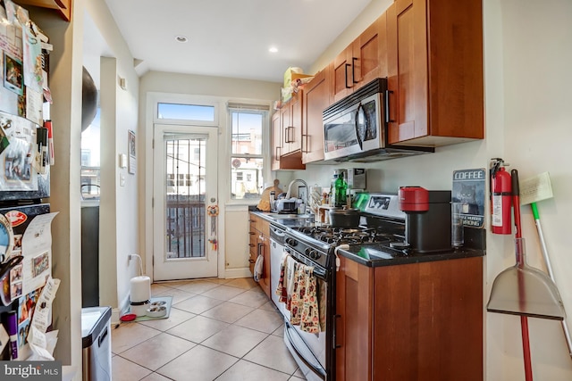 kitchen with appliances with stainless steel finishes, brown cabinetry, light tile patterned flooring, and a sink