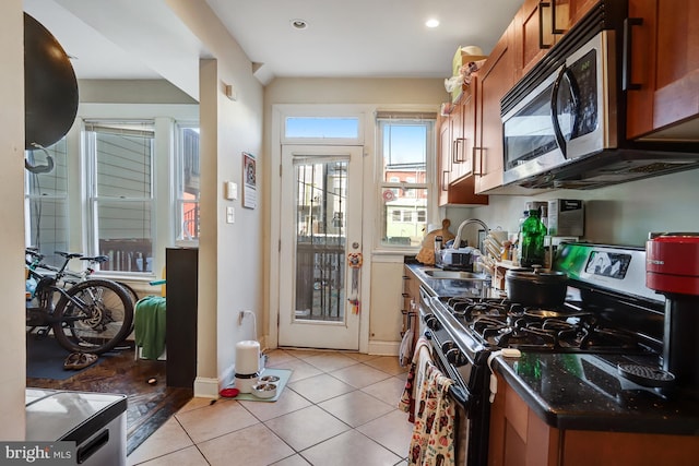 kitchen with light tile patterned floors, a sink, baseboards, appliances with stainless steel finishes, and brown cabinetry