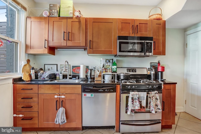 kitchen with stainless steel appliances, brown cabinets, a sink, and light tile patterned flooring