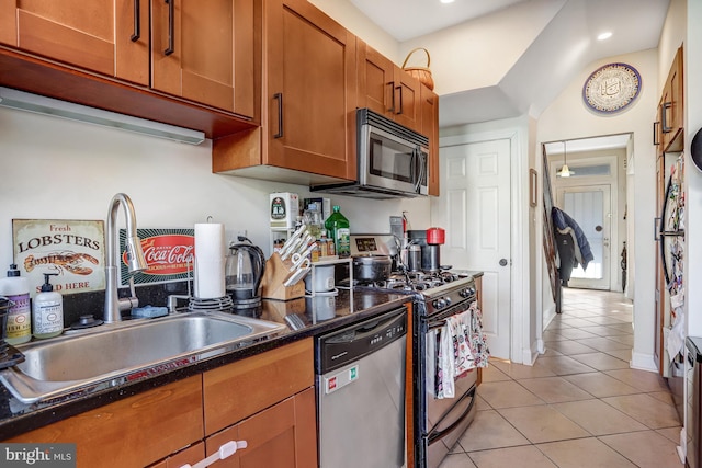 kitchen with light tile patterned floors, stainless steel appliances, a sink, brown cabinetry, and dark countertops