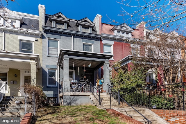 view of front of house featuring mansard roof, a chimney, stairway, covered porch, and brick siding