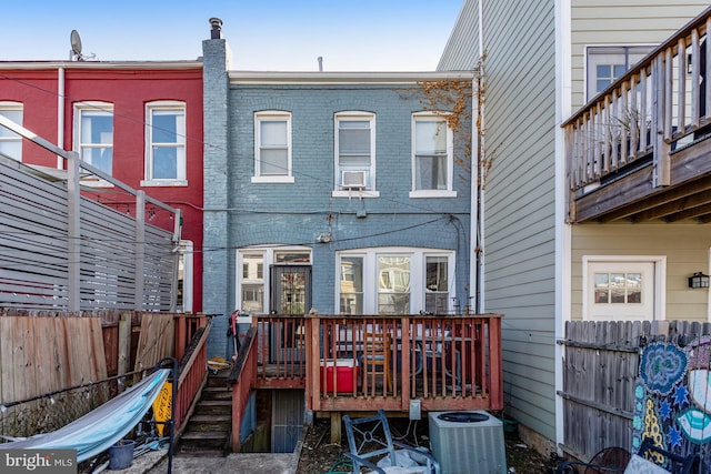 rear view of property featuring central air condition unit, fence, a deck, and brick siding