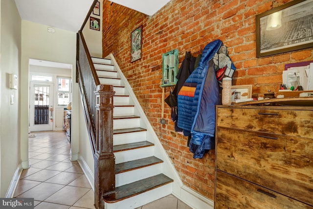 stairway with brick wall, baseboards, and tile patterned floors