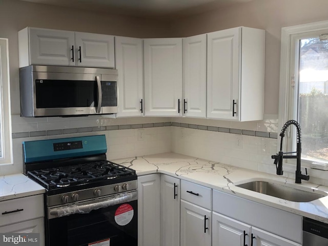 kitchen with white cabinets, a sink, light stone countertops, stainless steel appliances, and backsplash