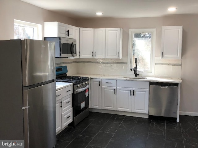 kitchen with a sink, marble finish floor, stainless steel appliances, white cabinetry, and backsplash