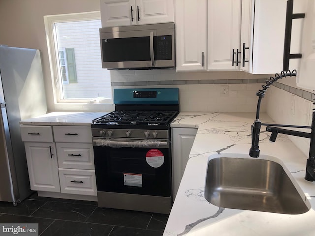 kitchen featuring stainless steel appliances, a sink, white cabinetry, backsplash, and light stone countertops