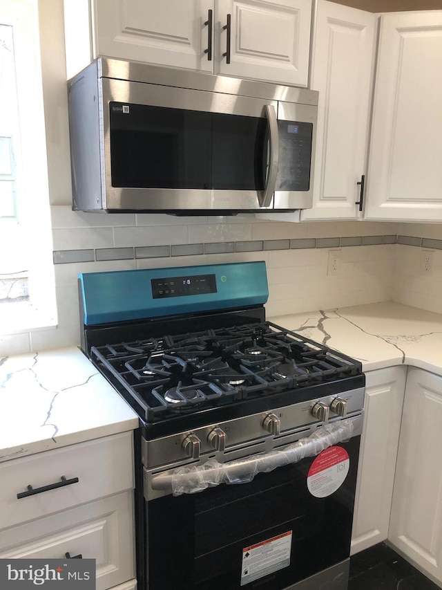 kitchen featuring tasteful backsplash, white cabinetry, stainless steel appliances, and light stone counters