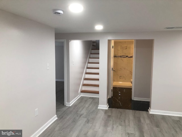 finished basement with visible vents, light wood-style flooring, baseboards, and stairs