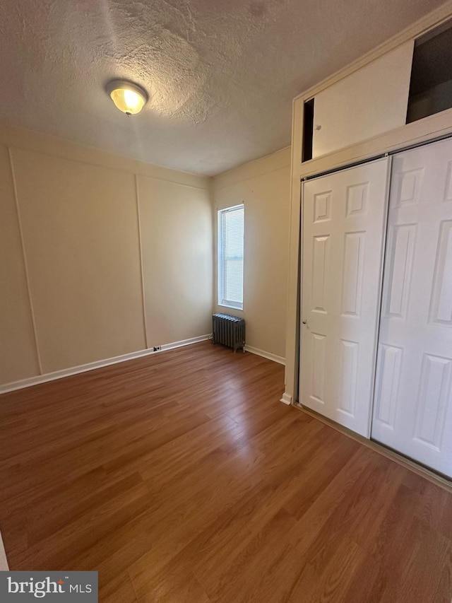 unfurnished bedroom with a textured ceiling, wood finished floors, baseboards, a closet, and radiator heating unit