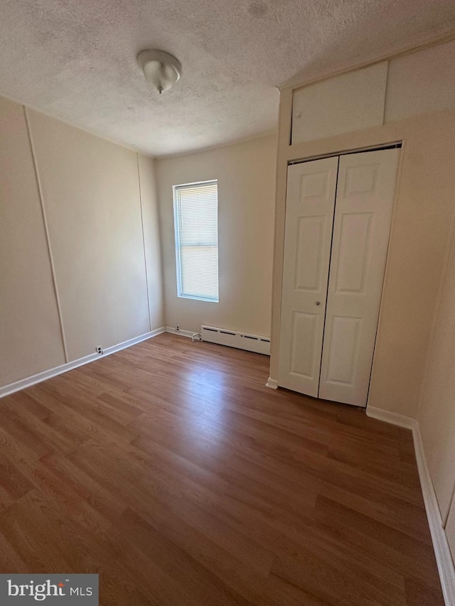 unfurnished bedroom featuring a textured ceiling, wood finished floors, and a baseboard radiator