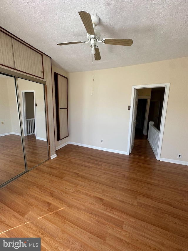 unfurnished bedroom featuring ceiling fan, a textured ceiling, baseboards, a closet, and light wood-style flooring