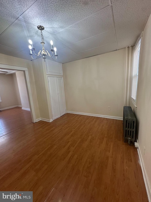 interior space featuring wood finished floors, a drop ceiling, radiator heating unit, and a notable chandelier