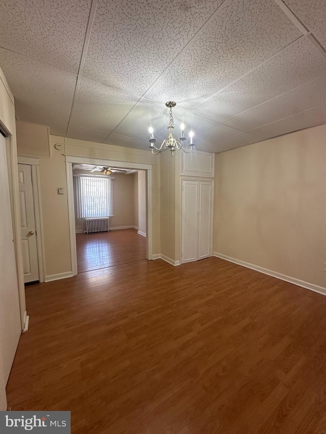 unfurnished dining area featuring baseboards, radiator, ceiling fan with notable chandelier, and wood finished floors
