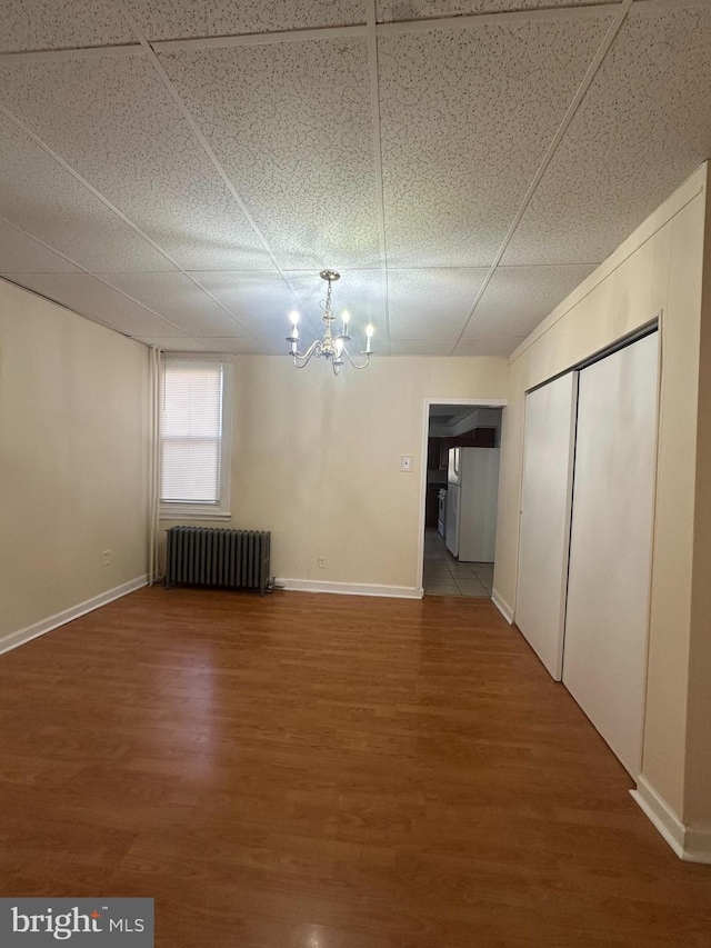 unfurnished dining area featuring baseboards, an inviting chandelier, radiator heating unit, and wood finished floors