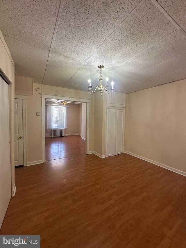 spare room featuring wood finished floors, baseboards, radiator heating unit, and a chandelier