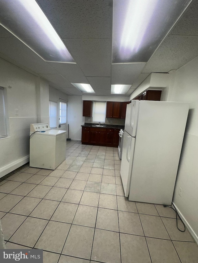kitchen with baseboards, freestanding refrigerator, washer / dryer, and light tile patterned floors