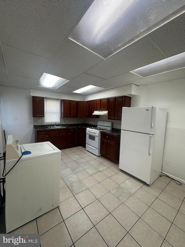 kitchen with dark countertops, white appliances, a paneled ceiling, under cabinet range hood, and a sink