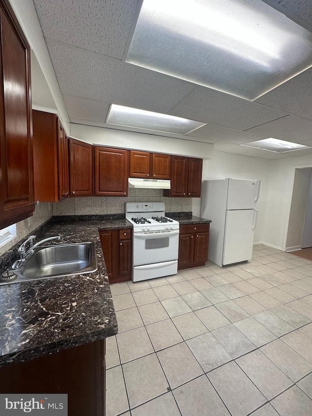 kitchen featuring white appliances, a paneled ceiling, under cabinet range hood, a sink, and light tile patterned floors