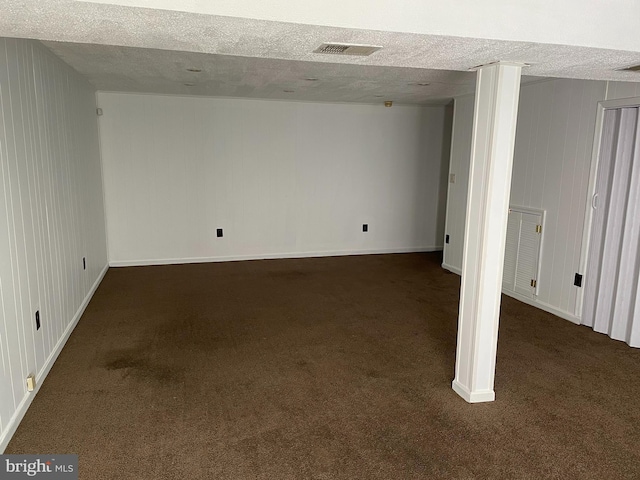 finished below grade area featuring visible vents, dark carpet, a textured ceiling, and baseboards