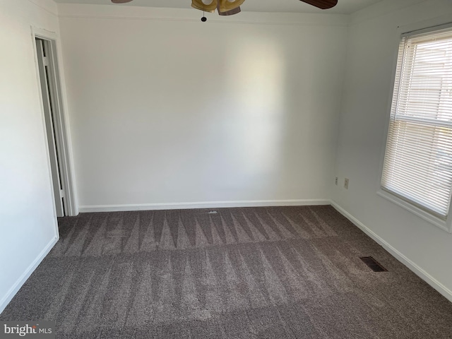 unfurnished room with baseboards, dark carpet, visible vents, and a ceiling fan