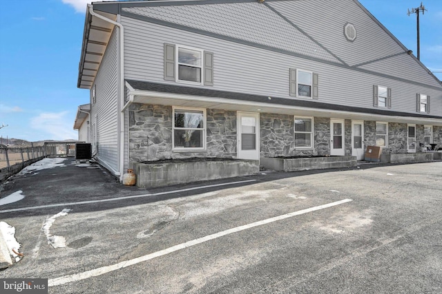 view of front of property featuring covered porch, stone siding, and central AC