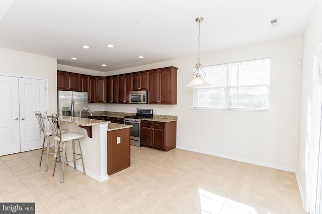 kitchen featuring light stone counters, recessed lighting, stainless steel appliances, an island with sink, and pendant lighting