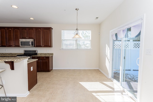 kitchen with dark brown cabinetry, appliances with stainless steel finishes, light stone counters, a kitchen bar, and pendant lighting