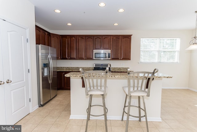 kitchen featuring stainless steel appliances, decorative light fixtures, a center island with sink, and light stone countertops