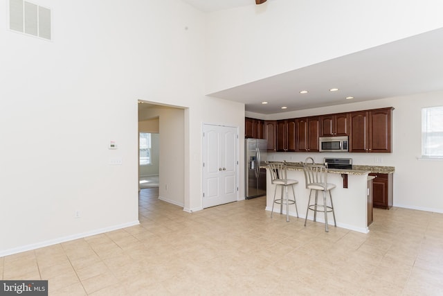 kitchen featuring stainless steel appliances, visible vents, a kitchen breakfast bar, light stone countertops, and a center island with sink