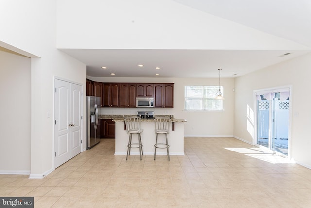 kitchen with light stone counters, a breakfast bar area, a kitchen island, appliances with stainless steel finishes, and pendant lighting