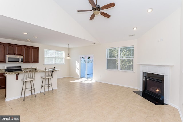 kitchen featuring light stone counters, stainless steel appliances, a breakfast bar, a fireplace with flush hearth, and open floor plan