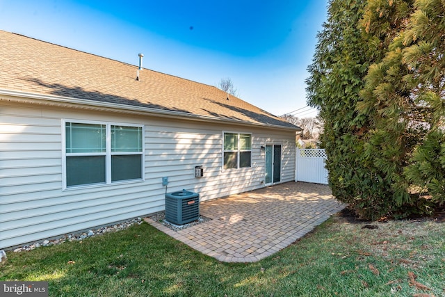 back of property featuring roof with shingles, a yard, a patio area, central AC, and fence