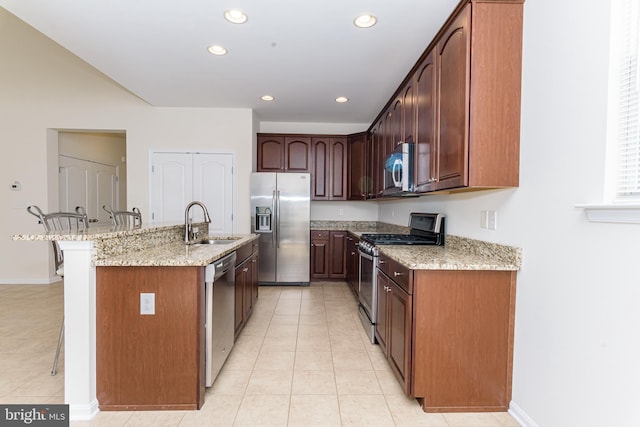 kitchen with a kitchen island with sink, stainless steel appliances, a breakfast bar, a sink, and light stone countertops