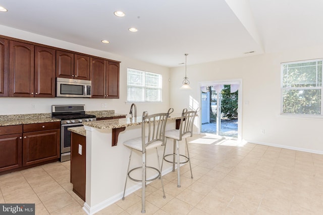 kitchen with light stone counters, appliances with stainless steel finishes, an island with sink, a kitchen bar, and decorative light fixtures