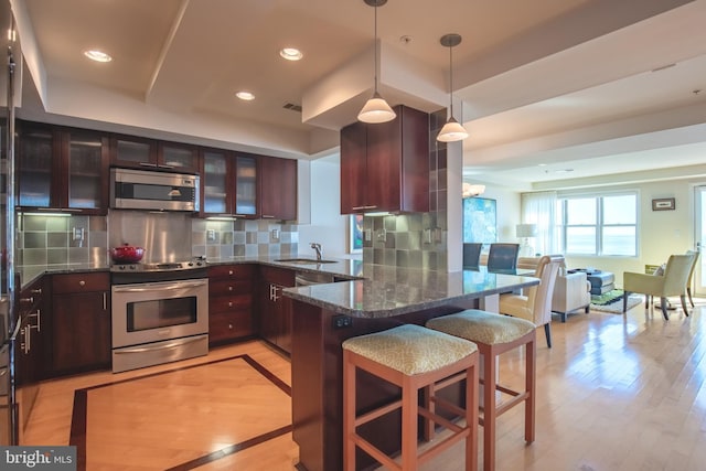 kitchen featuring light wood finished floors, tasteful backsplash, appliances with stainless steel finishes, open floor plan, and a sink