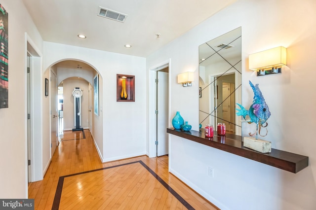 hallway with arched walkways, light wood-type flooring, visible vents, and recessed lighting